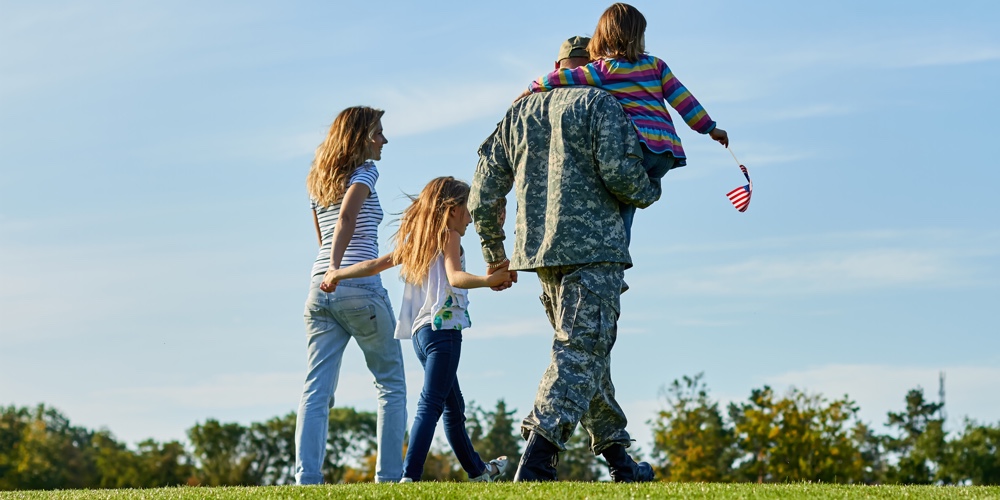 Back view soldier and his family are walking on the grass.