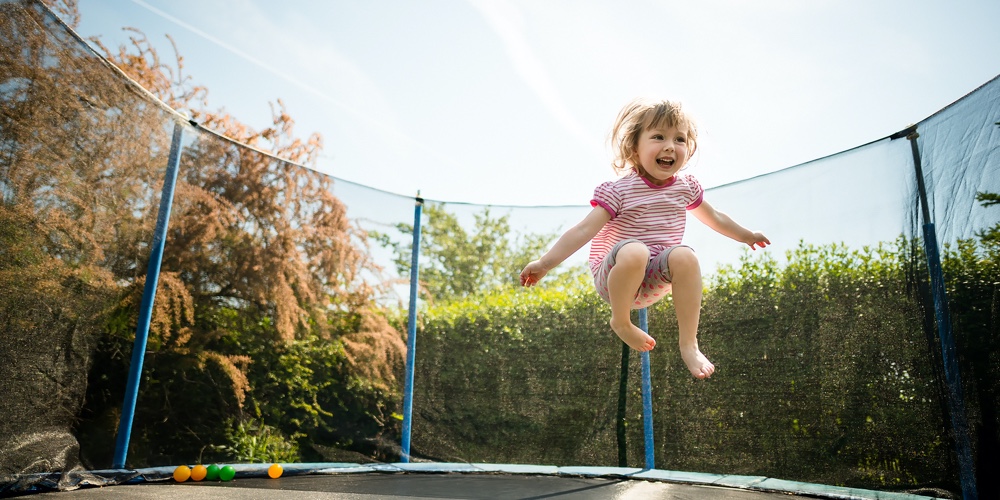 Little child enjoys jumping on trampoline – outside in backyard