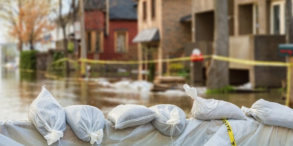 cuaidapp|Close shot of flood Protection Sandbags with flooded homes in the background