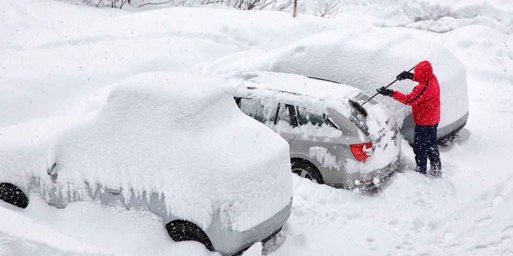 Young attractive man brushing the snow off his car on a cold winter day