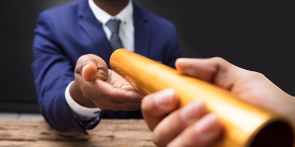 Close-up Of A Businessman’s Hand Passing Golden Relay Baton To His Partner