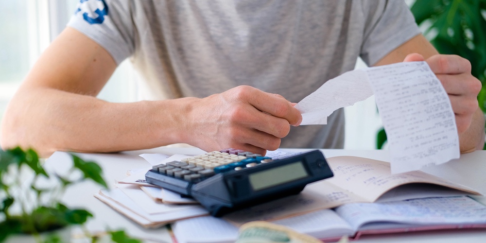 A Man Counts A Bill On A Calculator On The Table. Payment Of Utility Services. Saving Energy And Mon