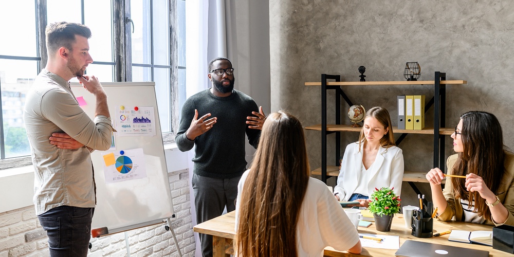 A Team Of Young And Successful Employees Listen To Progress Report From Male Afro-american Employee