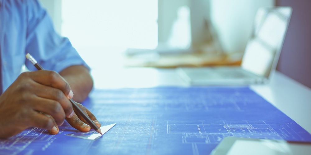 African American Architect Working With Computer And Blueprints In Office