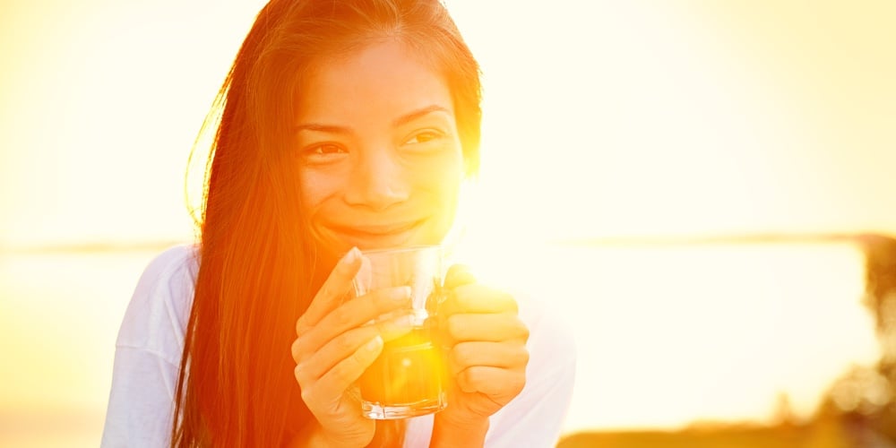 Asian woman drinking coffee in sun sitting outdoor in sunshine light enjoying her morning coffee. Sm