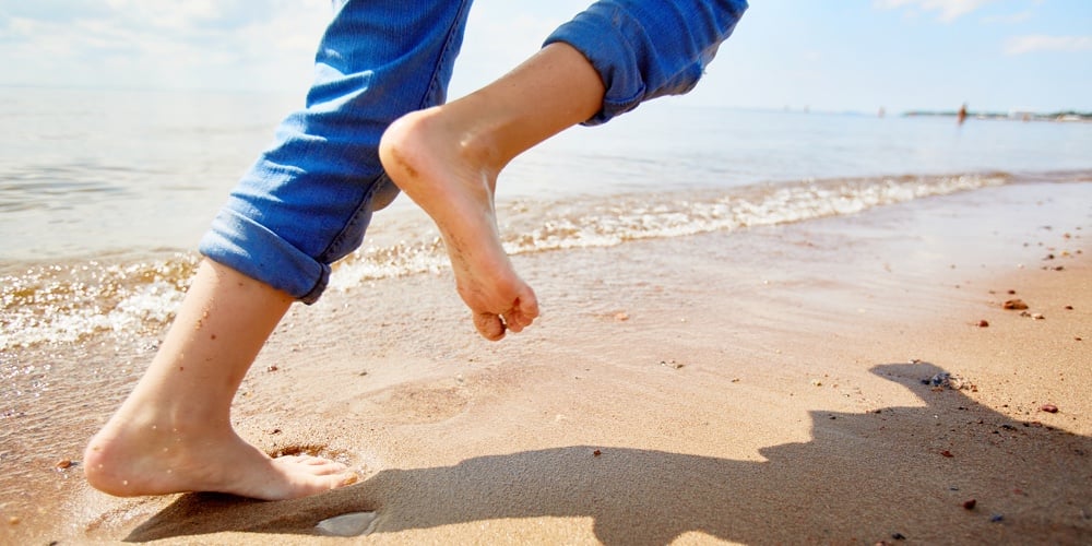 Barefoot child running on sandy beach along coastline while enjoying summer vacation or weekend