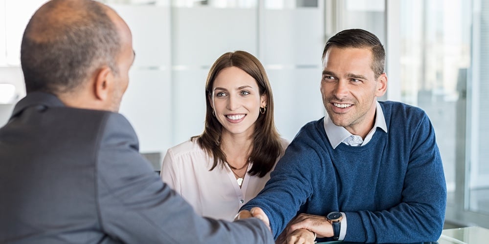 Businessman shaking hand with a young couple in office. Bank agent and his client shaking hands in c