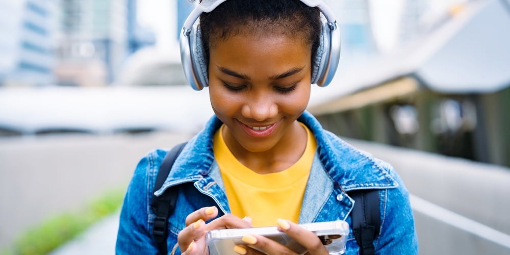 Cheerful Black Student Girl Wearing Headset And Using Mobile Smartphone