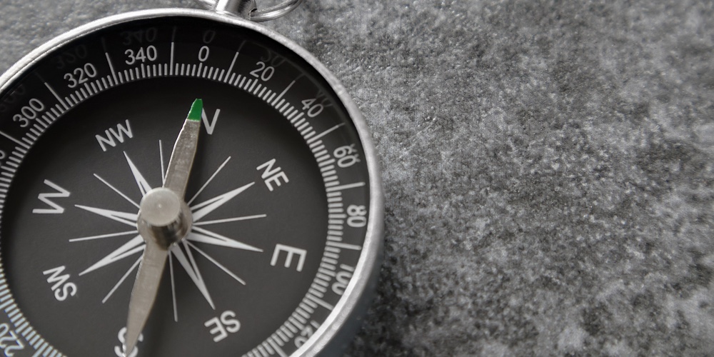 Close Up Of Magnetic Compass With Black Dial Laying On Stone Surface And Arrow Pointing North