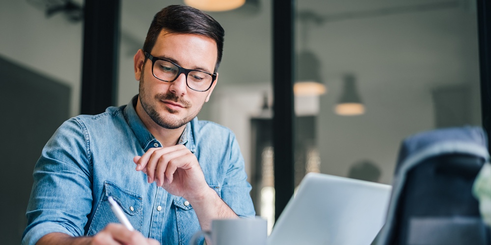 Close Up Portrait Of Handsome Man Working From Home Office Taking Reading And Writing Notes In Note