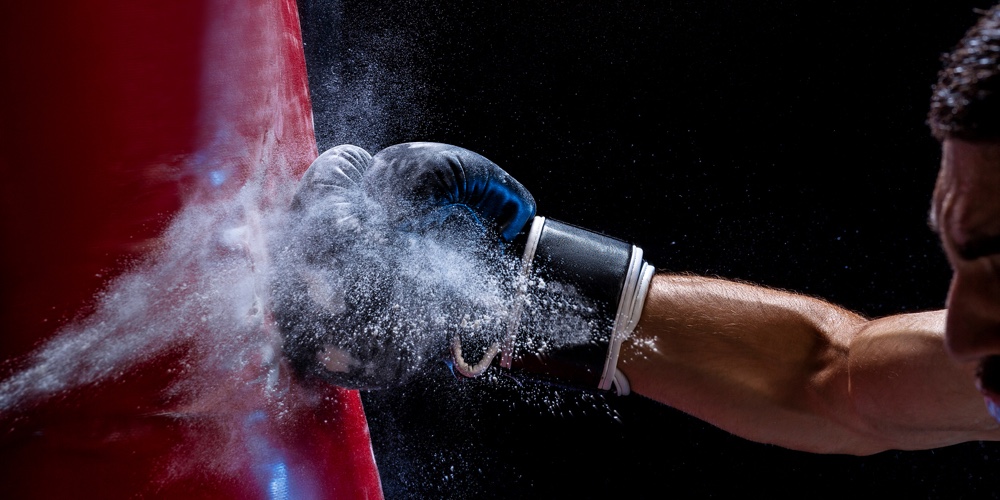 Close-up Hand Of Boxer At The Moment Of Impact On Punching Bag Over Black Background. Strength And M
