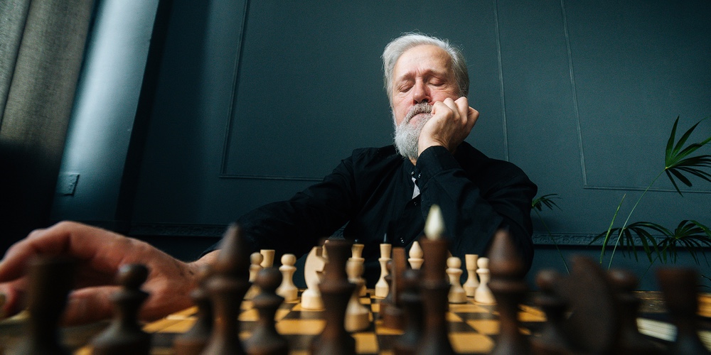 Close-up Low-angle View Of Pensive Gray-haired Senior Aged Man Thinking Game Strategy Sitting On Woo