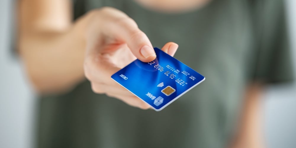 Cover_+_Graph_Image|Close up of young woman hand holding credit card. Woman extending hand to give credit card to cashie