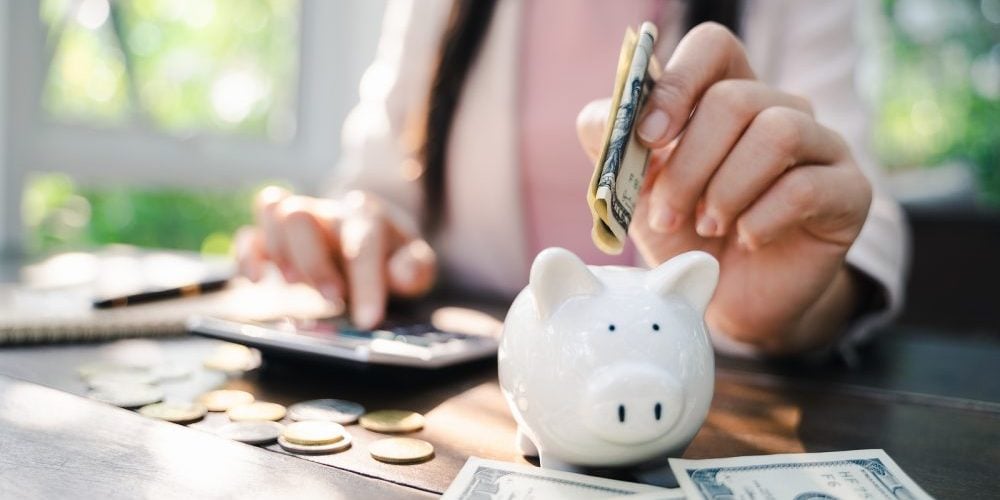 Closeup Of Business Woman Hand Putting Money Into Piggy Bank For