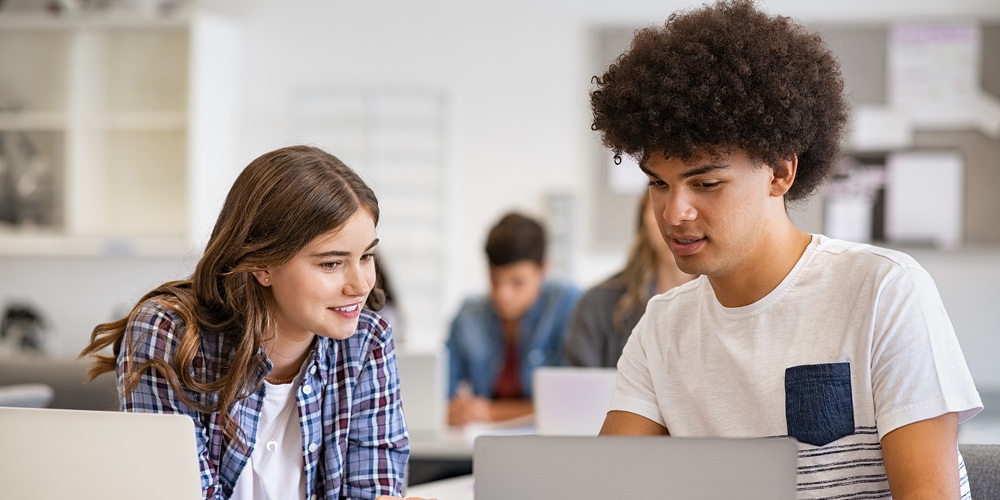 College students sitting together and using laptop during computer lesson. Black man and girl workin