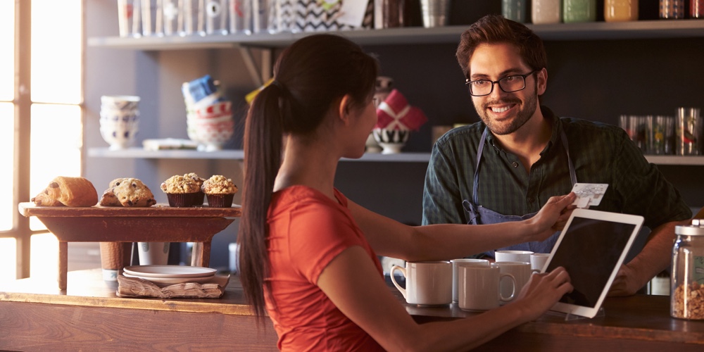 Customer In Coffee Shop Paying Using Digital Tablet Reader