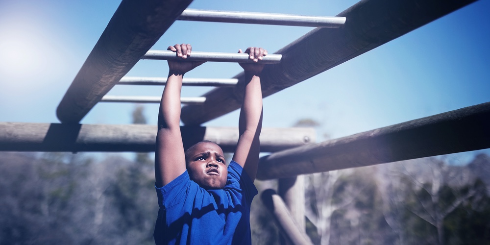 Determined boy exercising on monkey bar during obstacle course in boot camp
