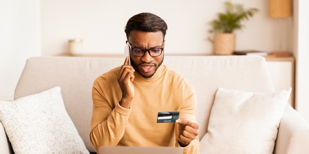 Discontented Black Man Calling To Bank Solving Problems With Credit Card Shopping Online On Laptop A