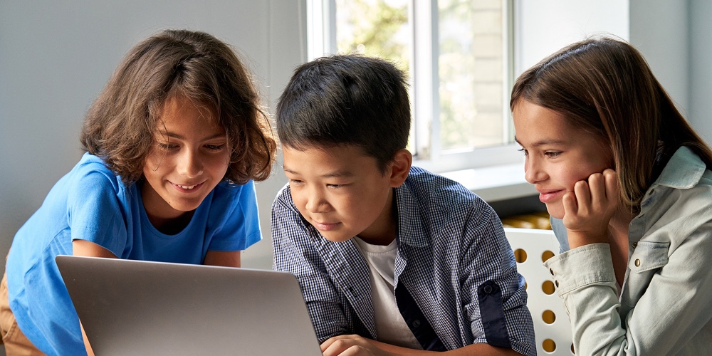 TES_young|Diverse Happy School Kids Using Laptop Computer Together In Classroom. Multicultural Children Junior