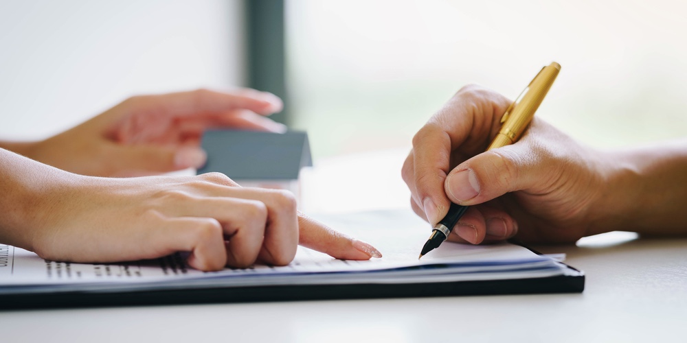 Estate Agent Pointing Finger On Document Showing Where To Sign. Signing A Paper Document For Buying