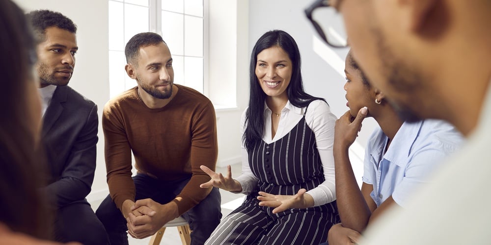 Female Coach Or Team Leader Tells Funny Story Or Joke To Diverse Team During Work Meeting.