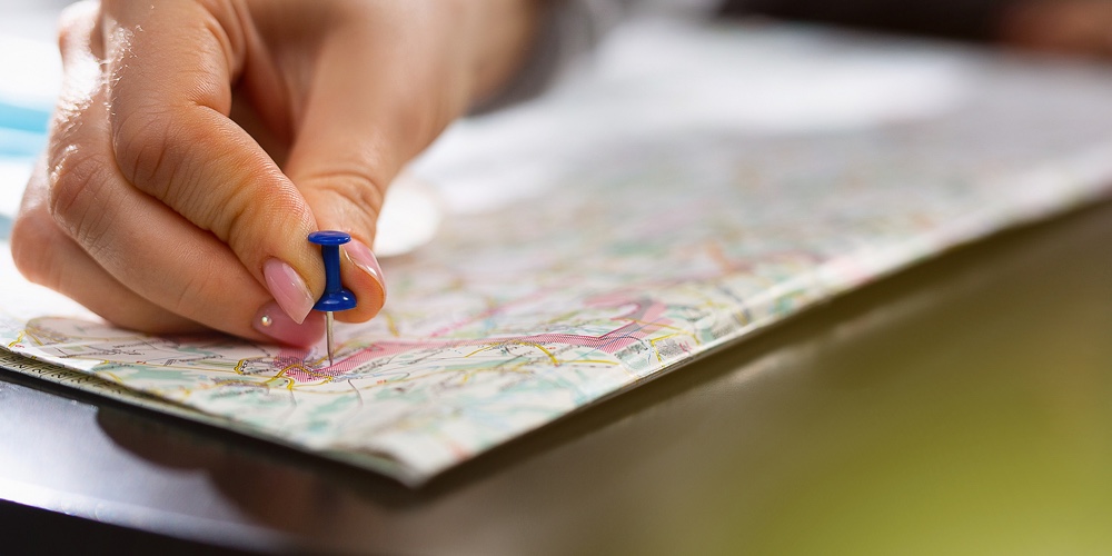 Female Hand Holding Pushpin Showing The Location Of A Destination Point On A Map. Travel Destination
