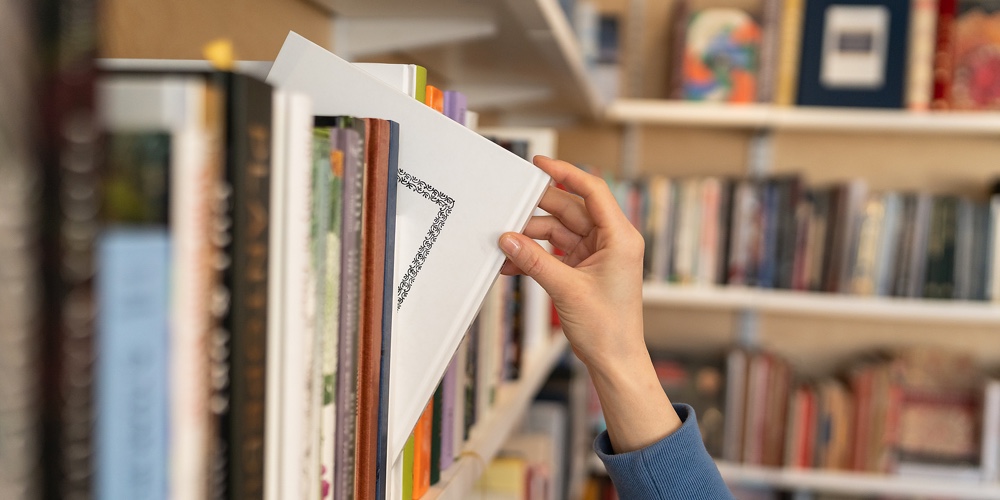 Female Hand Pulling Book From Bookshelf In Public Library In University