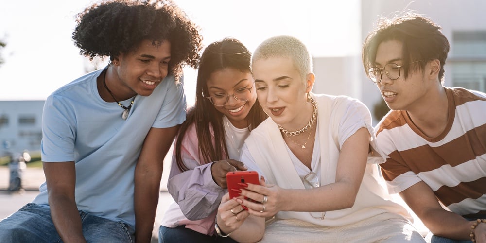 Group Of Gen Z Friends Sitting Together Using Mobile Phones To Share Content On Social Media