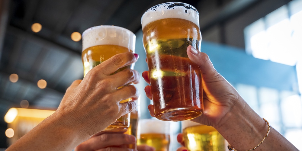 Group Of Women Toasting With Glasses Of Beer In A Pub. Close-up On The Hands And The Jugs Of Beer