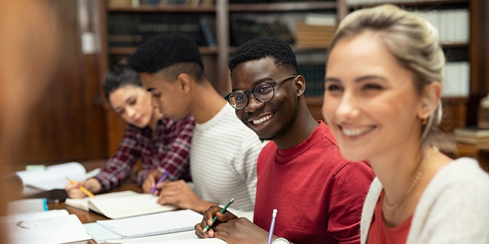 Group of happy multiethnic students studying and writing together in a library. College students in