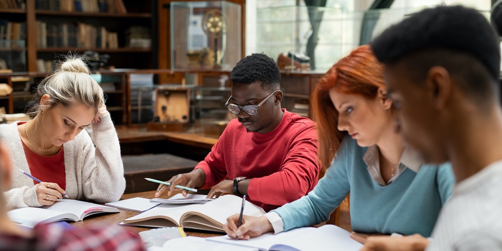 Group of university students doing class assignment in the library. Multiethnic young men and women