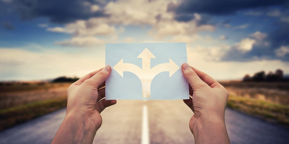 Hands Holding Paper With Arrows Crossroad Symbol Splitted In Three Different Directions. Choose The