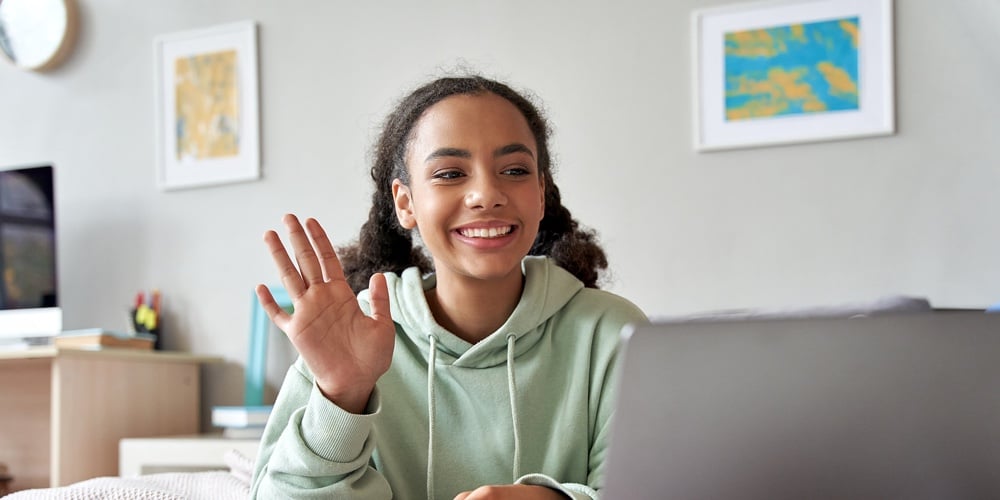 Happy African Gen Z Teen Girl Waving Hand Video Calling On Laptop At Home. Mixed Race Teenager Chatt