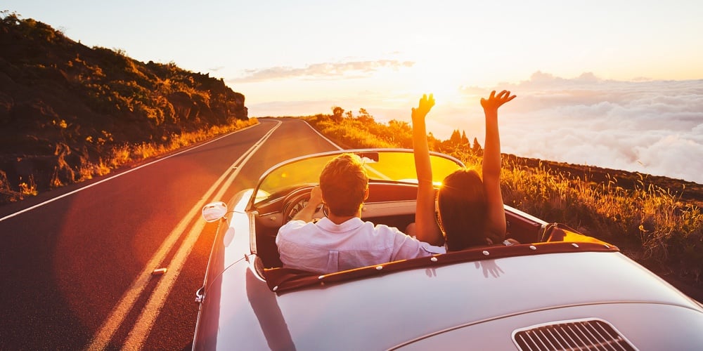 Happy Couple Driving on Country Road into the Sunset in Classic Vintage Sports Car