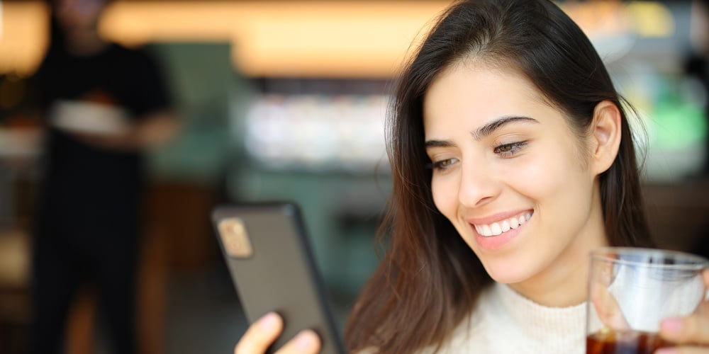 Happy Customer Checking Cell Phone Holding Soda In A Restaurant