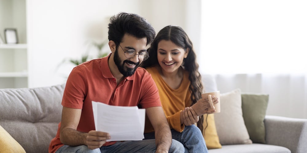 Happy Indian Spouses Checking Financial Documents And Calculating Family Budget At Home