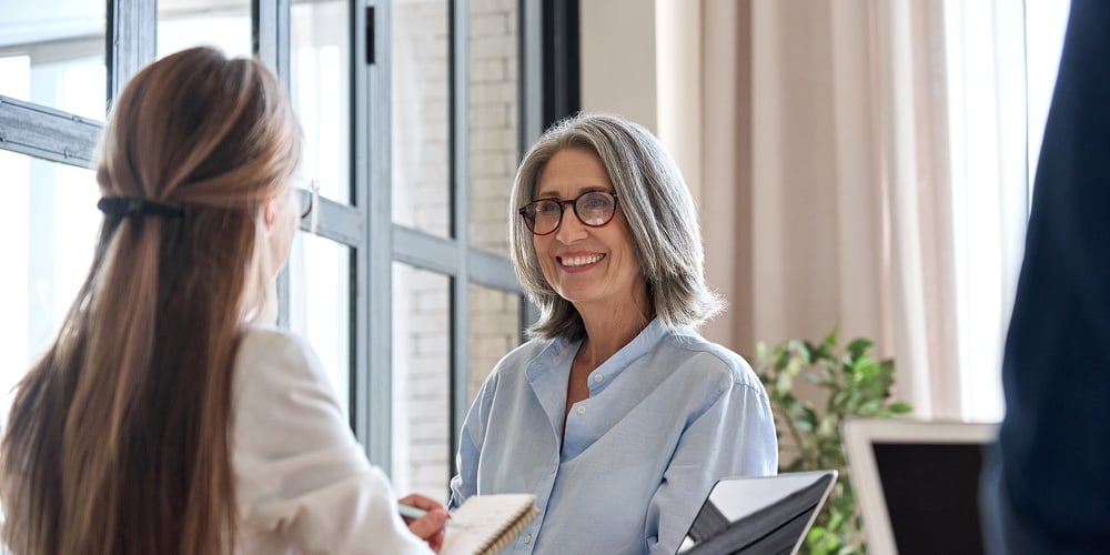 Happy Mature Middle 60s Aged Smiling Lady Boss Manager Teacher Talking To Assistant Or Student Meeti