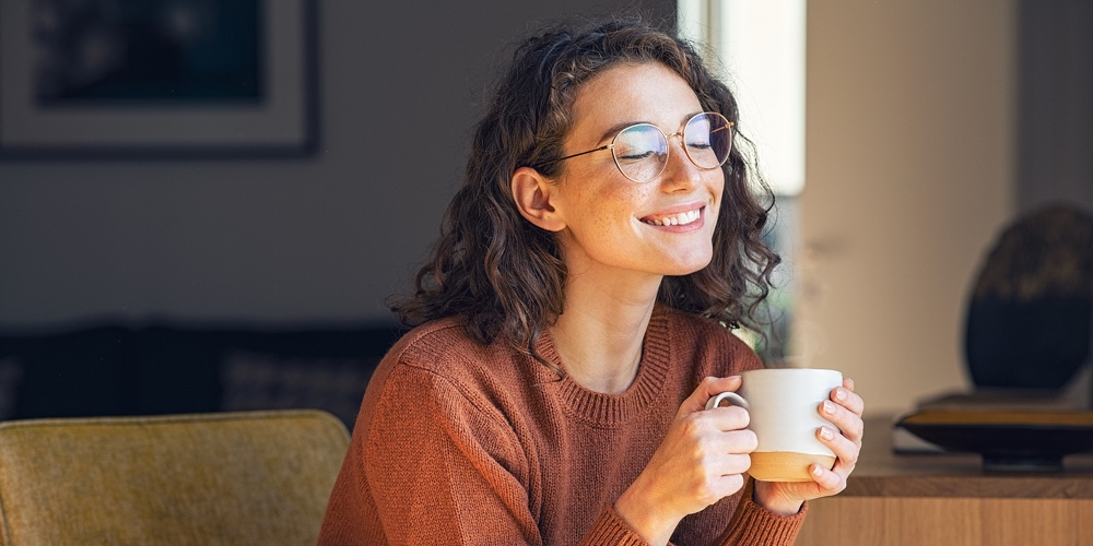 Happy young woman drinking a cup of tea in an autumn morning. Dreaming girl sitting in living room w