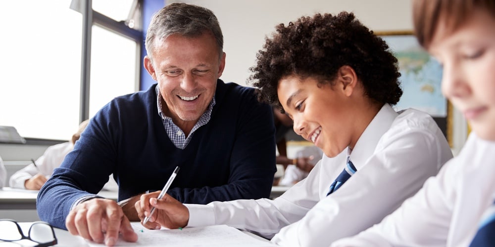 High School Tutor Giving Male Student Wearing Uniform One To One Tuition At Desk