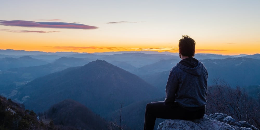 Hiker Sitting Alone On Top Of The Hill Waiting For Sunrise And Enjoying Scenic View Of Hills And Val