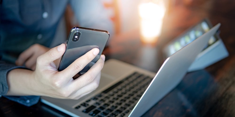 Male Hand Holding Smartphone. Businessman Using Laptop Computer And Digital Tablet While Working In