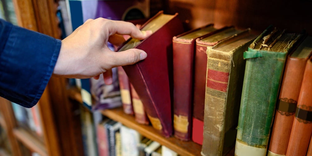 Male University Student Hand Choosing And Picking Vintage Book From Old Wooden Bookshelf In College