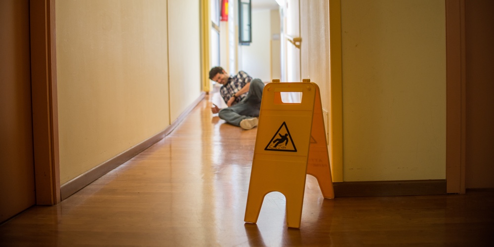 Man Slips On Wet Floor. Wet Floor Danger Sign In The Foreground. Concept Of Danger Slipping