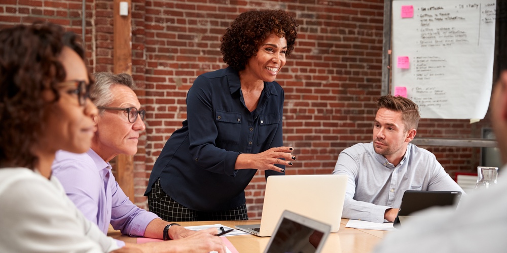 Mature Businesswoman Standing And Leading Office Meeting Around Table