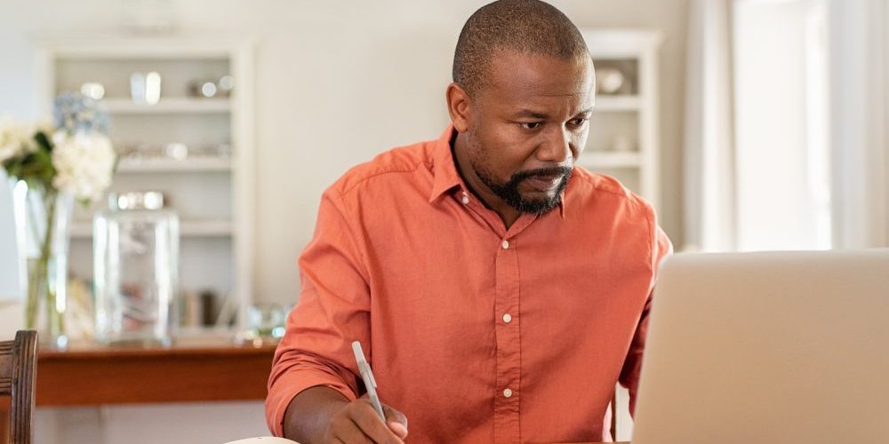 Mature man working on laptop while taking notes. Businessman wor