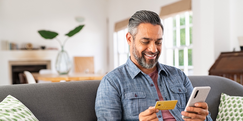 Middle eastern mature man using credit card to make online payment on smartphone. Mixed race man usi