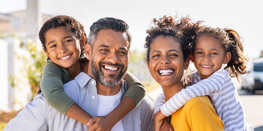 Mixed race parents giving piggyback ride to their children. Portrait of happy african mother and ind