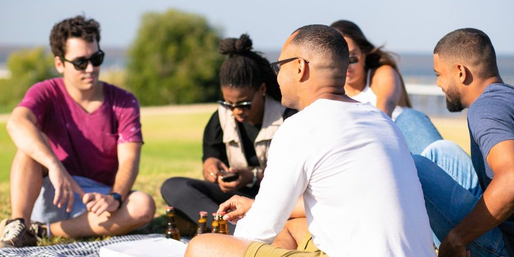Multiethnic Group Of Friends Meeting In Park For Picnic. Young M