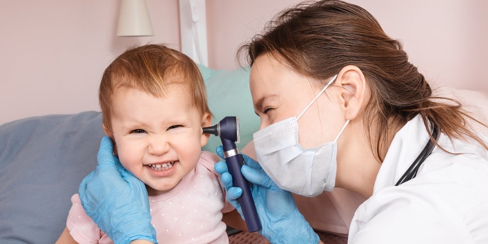 Pediatrician examines ear of baby girl at home during coronavirus COVID-19 pandemic quarantine. Doct