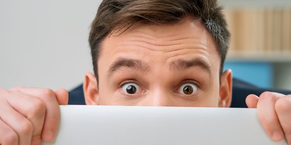 Pleasant office worker hiding behind laptop